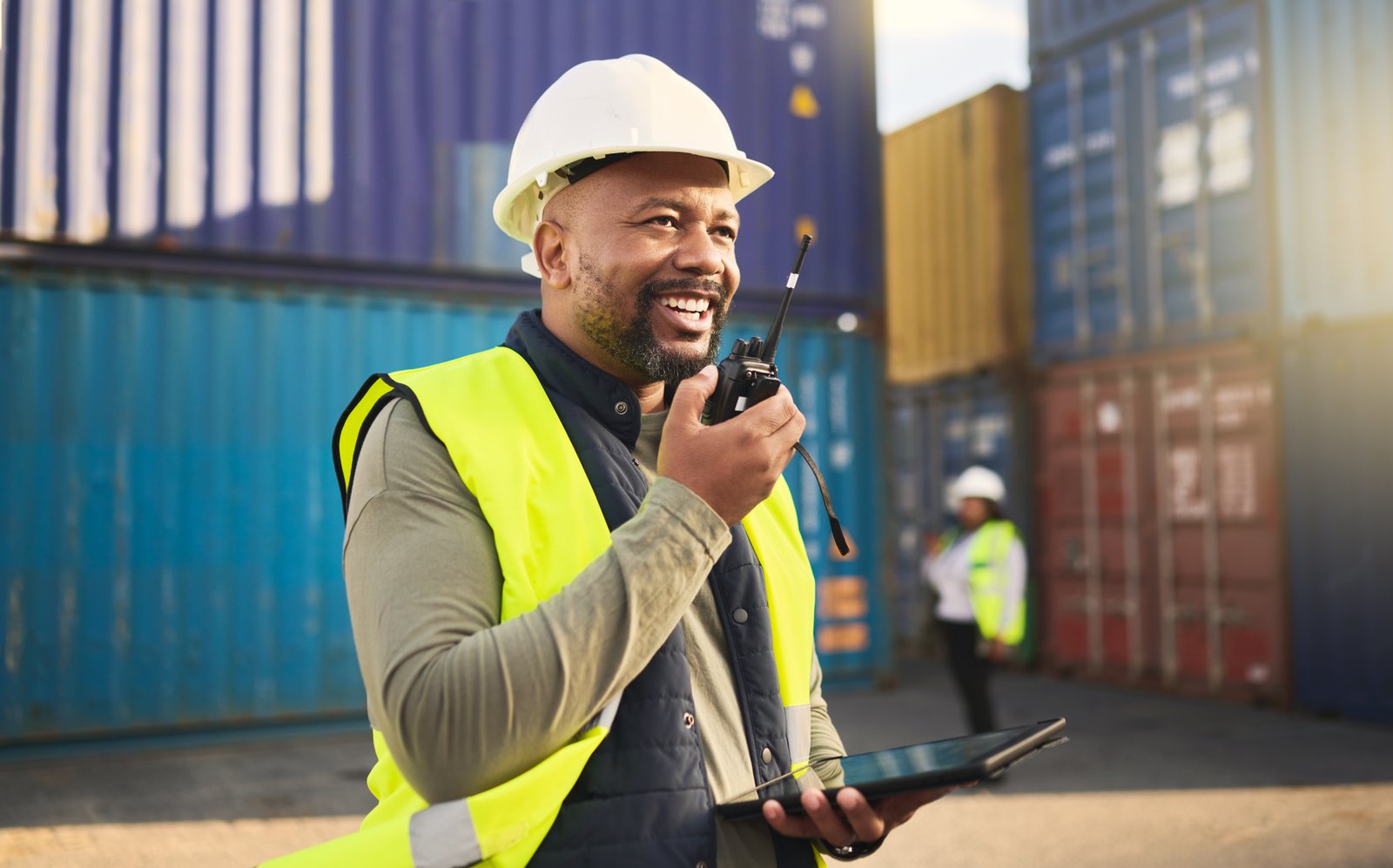 Logistics, radio and a black man in shipping container yard with tablet. Industrial cargo area, hap